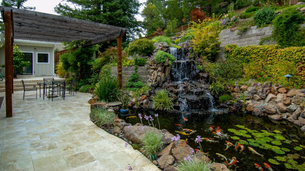 Tall waterfall and koi pond with block retaining walls and travertine patio