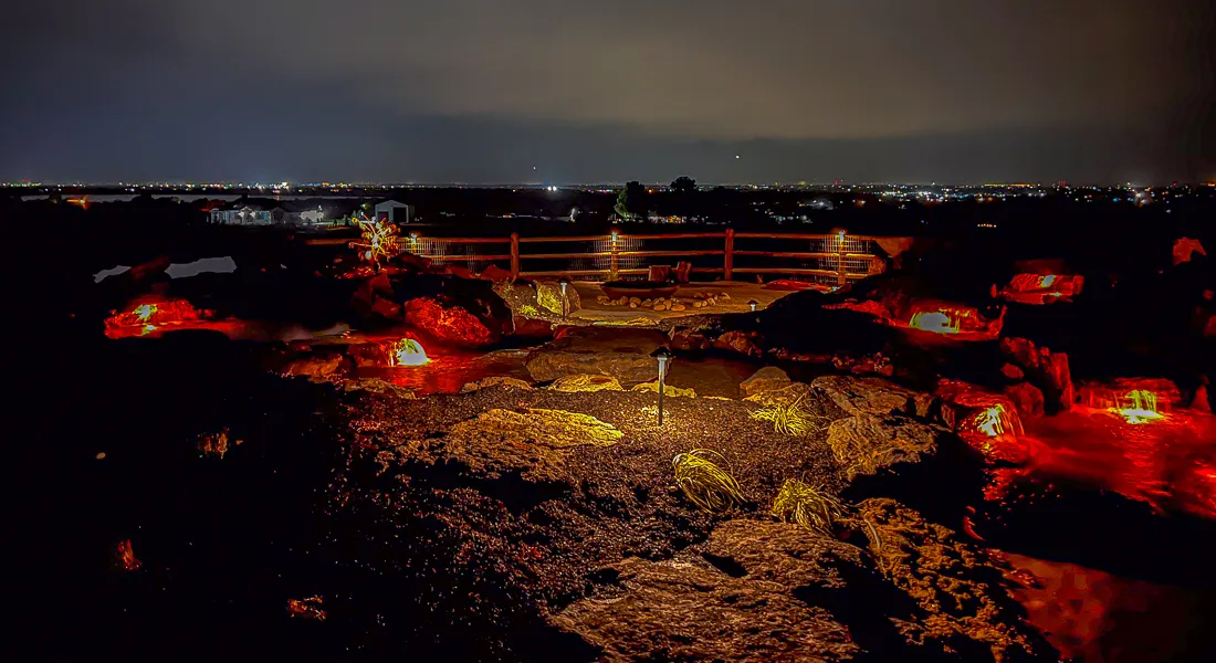 a fire pit with rocks and landscape lighting turned on at night showing a warm glow