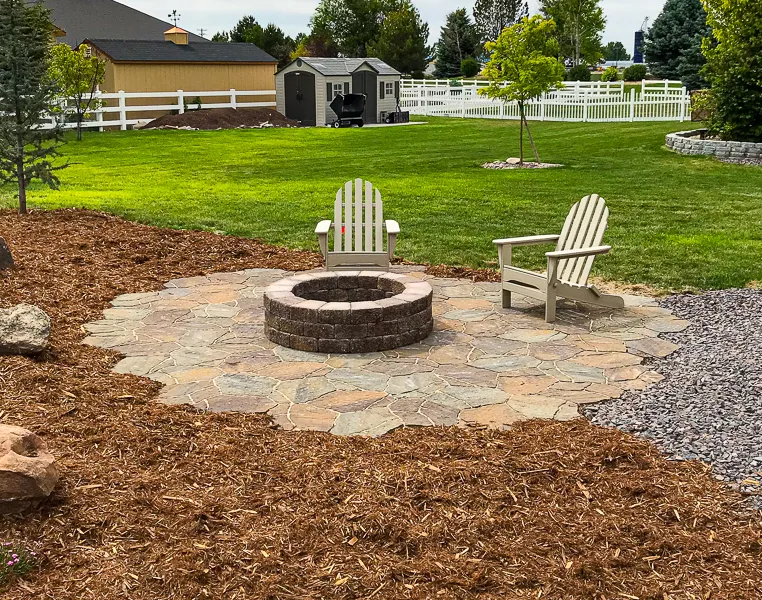 a fire pit on top of a paver patio with chairs in the middle of a yard in Meridian